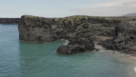 Aerial-flying-backwards-at-wild-coastal-terrain-of-Iceland-with-turquoise-water