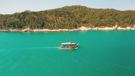 Side-aerial-view-of-a-tourist-boat-passing-by-on-turquoise-water-color-and-paradisiac-rainforest-scenery-sea