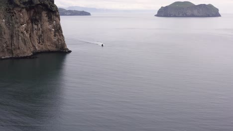 Speedboat-travels-past-rocky-cliff-with-Westman-Islands-of-Iceland-in-background