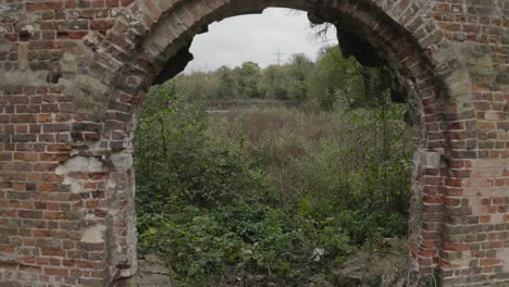 Flying-through-derelict-building-archway-with-green-foliage-behind