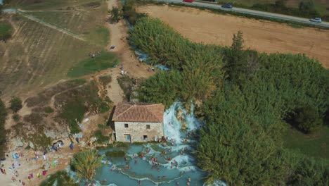 Aerial-footage-of-the-famous-Saturnia-Cascate-del-Mulino-thermal-hot-springs-with-its-blue-warm-water-near-Grosseto-in-the-idyllic-landscape-of-Tuscany,-Italy-with-olive-trees-and-fields-around