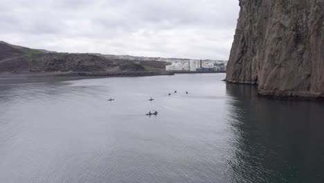 People-in-kayaks-next-to-large-rocky-cliffs-of-island-in-Atlantic-Ocean,-aerial