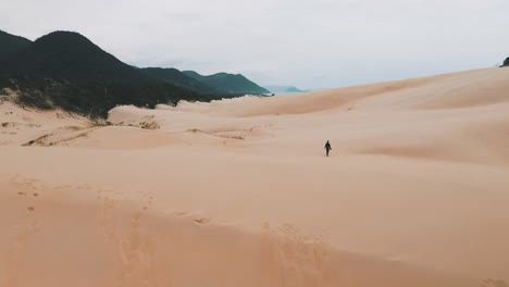Sandboarder-walking-on-sand-dunes-at-Garopaba-Beach,-Santa-Catarina,-Brazil