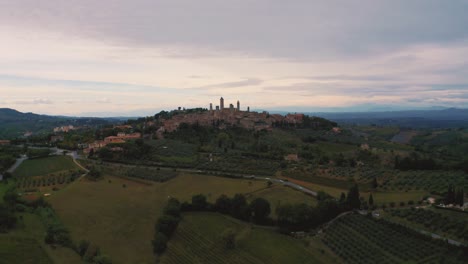 Aerial-drone-footage-of-the-medieval-town-San-Gimignano-near-Siena,-a-masterpiece-of-historic-architecture-in-the-idyllic-landscape-of-Tuscany,-Italy-with-vineyards,-hills-and-olive-trees-around