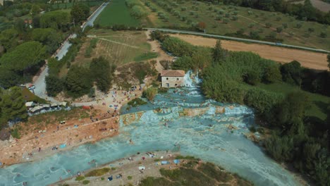 Aerial-drone-footage-of-the-iconic-Saturnia-Cascate-del-Mulino-thermal-hot-springs-with-its-blue-warm-water-near-Pitigliano-in-the-idyllic-landscape-of-Tuscany,-Italy-with-hills-and-olive-trees-around