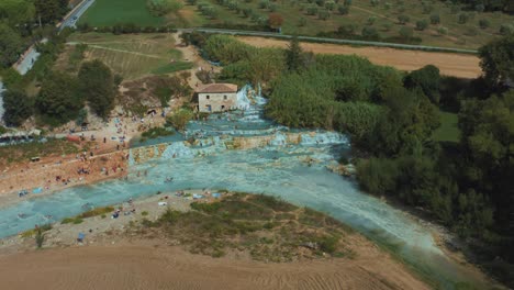 Drone-footage-of-the-famous-Saturnia-Cascate-del-Mulino-thermal-hot-springs-with-its-blue-warm-water-near-Grosseto-in-the-idyllic-landscape-of-Tuscany,-Italy-with-people,-fields-and-olive-trees-around