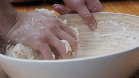 Chef-molds-the-pizza-dough-in-a-deep-plate,-on-a-wooden-table