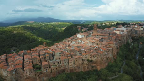 Aerial-drone-footage-of-the-ancient-medieval-town-Pitigliano,-a-masterpiece-of-historic-architecture-on-a-natural-rock-in-the-idyllic-landscape-of-Tuscany,-Italy-with-green-trees-and-blue-hills-around