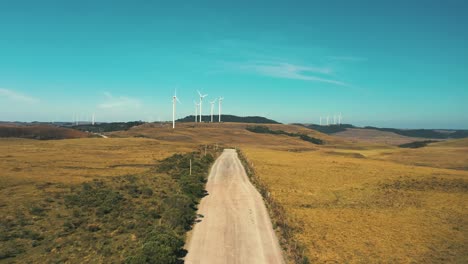 Drone-cinematic-shot-of-dirt-road-with-wind-turbine-generators-located-in-Santa-Catarina,-Brazil