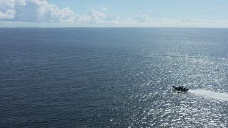 Speedboat-cruising-through-shimmering-blue-ocean-water,-Aerial-Tracking-Shot