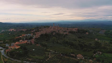 Beautiful-drone-footage-of-the-medieval-town-San-Gimignano-near-Siena,-a-masterpiece-of-historic-architecture-in-the-idyllic-landscape-of-Tuscany,-Italy-with-vineyards,-hills-and-olive-trees-around