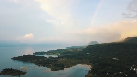 Beautiful-Drone-aerial-view-of-a-rainbow,-green-mountains-and-a-volcano-in-lake-Atitlan,-Guatemala
