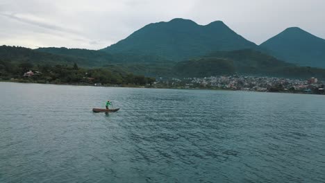 Drone-aerial-rotating-shot-of-a-man-paddling-on-a-boat-in-Lake-Atitlan,-Guatemala