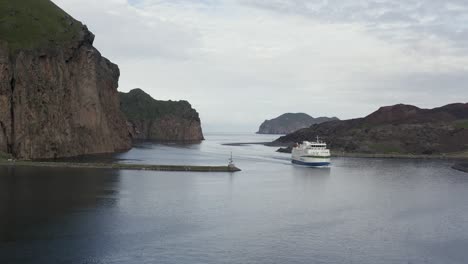 Ferry-arrives-in-Vestmannaeyjar-inlet-enclosed-by-amazing-rocky-cliffs,-Heimaey