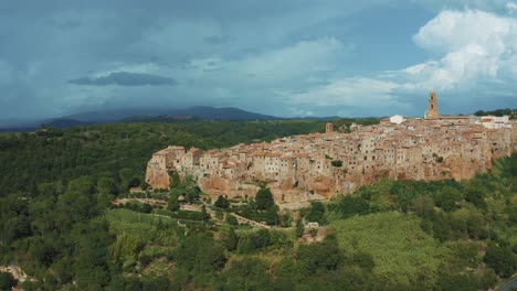 Aerial-drone-footage-of-the-historic-medieval-town-Pitigliano,-a-masterpiece-of-medieval-architecture-on-a-natural-rock-in-the-idyllic-landscape-of-Tuscany,-Italy-with-green-trees-and-blue-hills