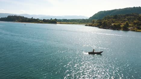 Einheimischer-Mann,-Der-Auf-Einem-Boot-Im-See-Atitlan,-Guatemala-Rudert---Drohnenluftaufnahme---Schöne-4k-landschaft