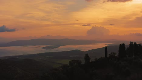 Aerial-drone-footage-of-the-iconic-Monte-Argentario-lagoon,-facing-the-ancient-old-town-Orbetello-close-to-the-Maremma-nature-park-in-Tuscany,-Italy-with-dramatic-clouds-covering-the-sky-at-sunrise