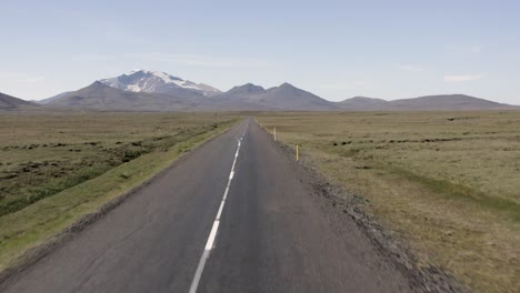 Antena-De-Vuelo-Bajo-Sobre-Camino-Rural-Vacío-En-Islandia-Con-Montañas-En-Segundo-Plano.