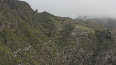 Impresionante-Camino-Sinuoso-De-Montaña-En-Terreno-Rocoso-Con-Follaje-Verde-Y-Nubes-Bajas-Que-Rozan-La-Cima-De-La-Montaña