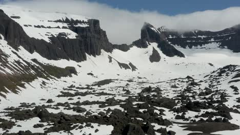Retroceso-Aéreo-De-Un-Gran-Dron-A-Través-De-Increíbles-Acantilados-De-Roca-Gris-Nevados-Islandeses-Y-Montañas-Cubiertas-De-Nubes