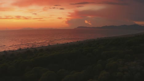 Beautiful-aerial-anamorphic-cinema-drone-footage-of-pine-tree-forest-and-sandy-beach-seaside-in-the-iconic-Maremma-nature-park-in-Tuscany,-Italy-with-dramatic-clouds-covering-the-sky-at-sunset