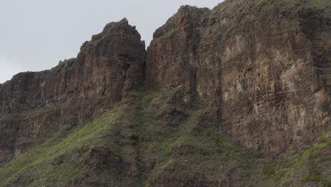 Dramatic-deep-brown-volcanic-rock-face-with-mossy-green-growth