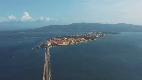 Aerial-drone-flight-above-the-old-town-Orbetello-island-close-to-Monte-Argentario-and-the-Maremma-Nature-Park-in-Tuscany,-Italy,-with-blue-sky-and-calm-blue-water