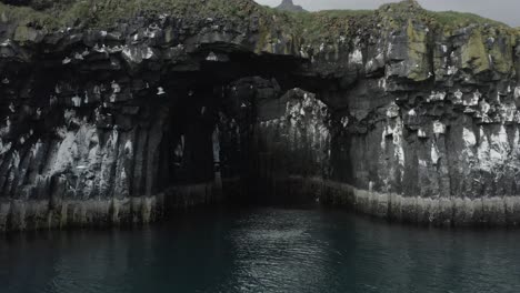 Incredible-low-angle-view-of-natural-stone-bridge-in-Iceland-with-birds,-aerial