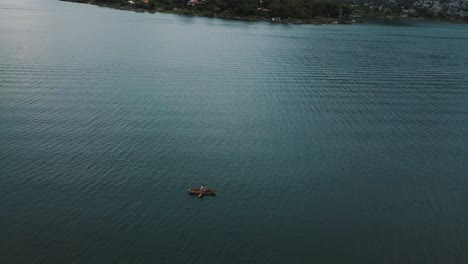 Drone-aerial-view,-local-fisherman-rowing-on-a-boat-in-Lake-atitlan,-Guatemala