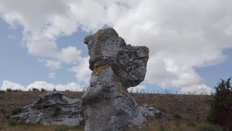 Rock-outcrop-in-natural-area-standing-out-against-sky-with-clouds,-arc-shot