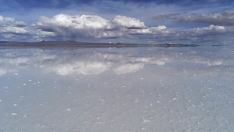 Stunning-mirror-effect-low-flying-drone-view-over-salt-flats-towards-light-clouds