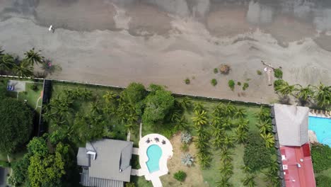 Aerial-top-down-view-tropical-beach-with-hotel-accomodation-and-lone-surfer