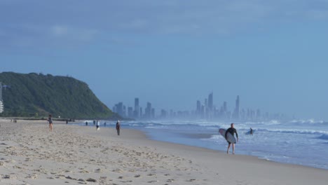 People-Enjoying-Palm-Beach---Surfers-Riding-Waves---Surfers-Paradise-On-The-Background---Gold-Coast,-Queensland,-Australia