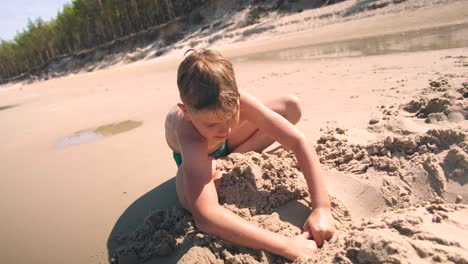 Young-boy-at-beach-is-busy-digging-a-hole-in-the-sand-with-shovel