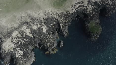 Filmische-Luft-über-Wilder-Küste-Mit-Dunklem-Vulkangestein-Neben-Sanftem-Ozean