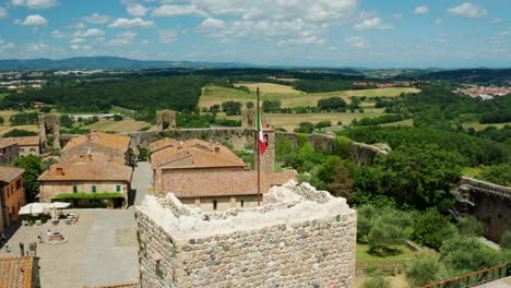 Ciudad-Medieval-De-Monteriggioni,-Bandera-Italiana-Sobrevolando-El-Fuerte