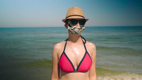 Young-woman-in-bikini-at-the-beach-puts-face-mask-on