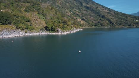 Drone-aerial-rotating-around-man-on-a-boat,-paddling-in-lake-Atitlan,-Guatemala,-Central-America