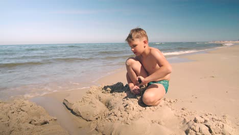 Young-boy-at-the-beach-is-busy-creating-a-path-into-the-sand-next-to-shoreline