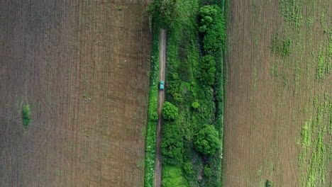 Car-driving-over-a-narrow-road-between-some-farm-fields