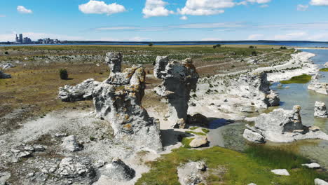 Drohnenansicht-Aus-Der-Vogelperspektive-Auf-Die-Ruhige-Ostsee-Und-Interessante-Felsformationen-An-Der-Küste-Der-Insel-Gotland-Mit-Einer-Stadt-Am-Horizont
