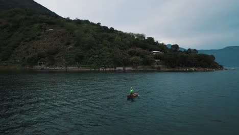 Cinematic-drone-aerial-shot-of-a-man-paddling-on-a-boat-in-Lake-Atitlan-Guatemala