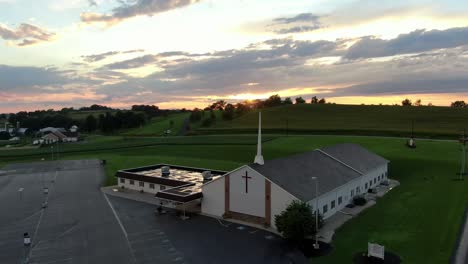 Aerial,-Christian-evangelical-church-with-steeple,-outside-of-building-and-dramatic-beautiful-sunrise,-sunset-in-the-heavenly-sky,-Lancaster-County-Pennsylvania