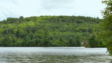 Timelapse---Clouds-Stir-Over-Forested-Hill-and-Choppy-Lake