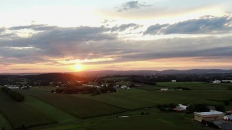 High-aerial-pullback-revealing-shot-of-rural-Lancaster-County-Pennsylvania-USA-farmland-under-dramatic-beautiful-sunset-sunrise,-rolling-hillside-countryside