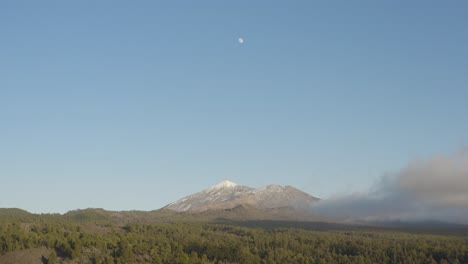 Impresionante-Vista-Sobre-El-Monte-Teide-Con-Luna,-Cielo-Azul-Y-Nubes-Rodeadas-De-Bosque-Verde