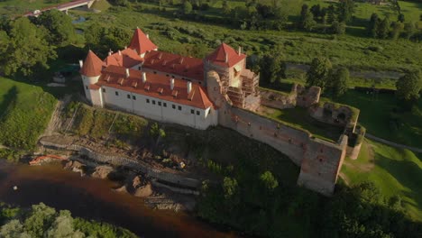 Drone-panorama-of-Bauska-castle-in-Latvia,-with-scaffolding-and-ruins-next-to-the-restored-castle