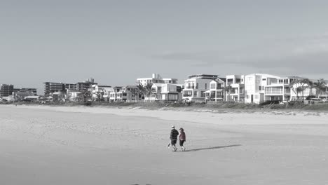 Black-And-White---Adult-Couple-Walking-Together-On-The-Sandy-Shore---Palm-Beach-Waterfront-Hotels-And-Apartments---Gold-Coast,-QLD,-Australia