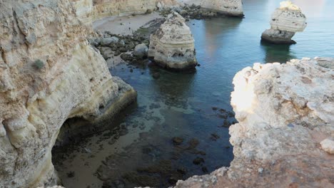 Kippen-Nach-Oben,-Malerischer-Blick-Auf-Den-Felstunnelstrand-An-Der-Algarve,-Portugal,-Menschen,-Die-Im-Hintergrund-An-Der-Küste-Spazieren-Gehen
