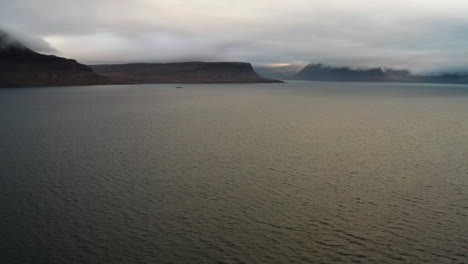 Aerial-shot-of-magical-fjord-and-hills-surrounded-by-clouds,-all-in-Westfjords